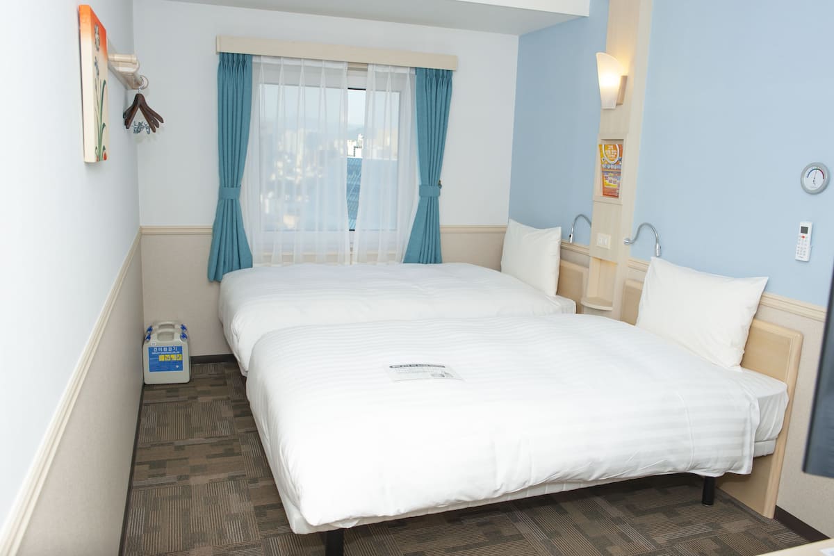 Une chambre d’hôtel avec un grand lit, une table de chevet, une fenêtre avec des rideaux, une horloge murale et une petite table de chevet avec une lampe.