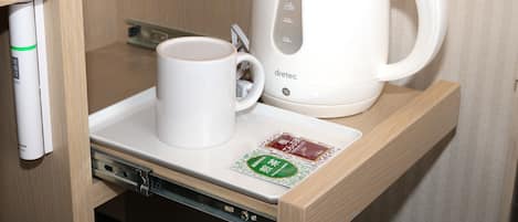 A white electric kettle and a white mug on a tray in a wooden cabinet.