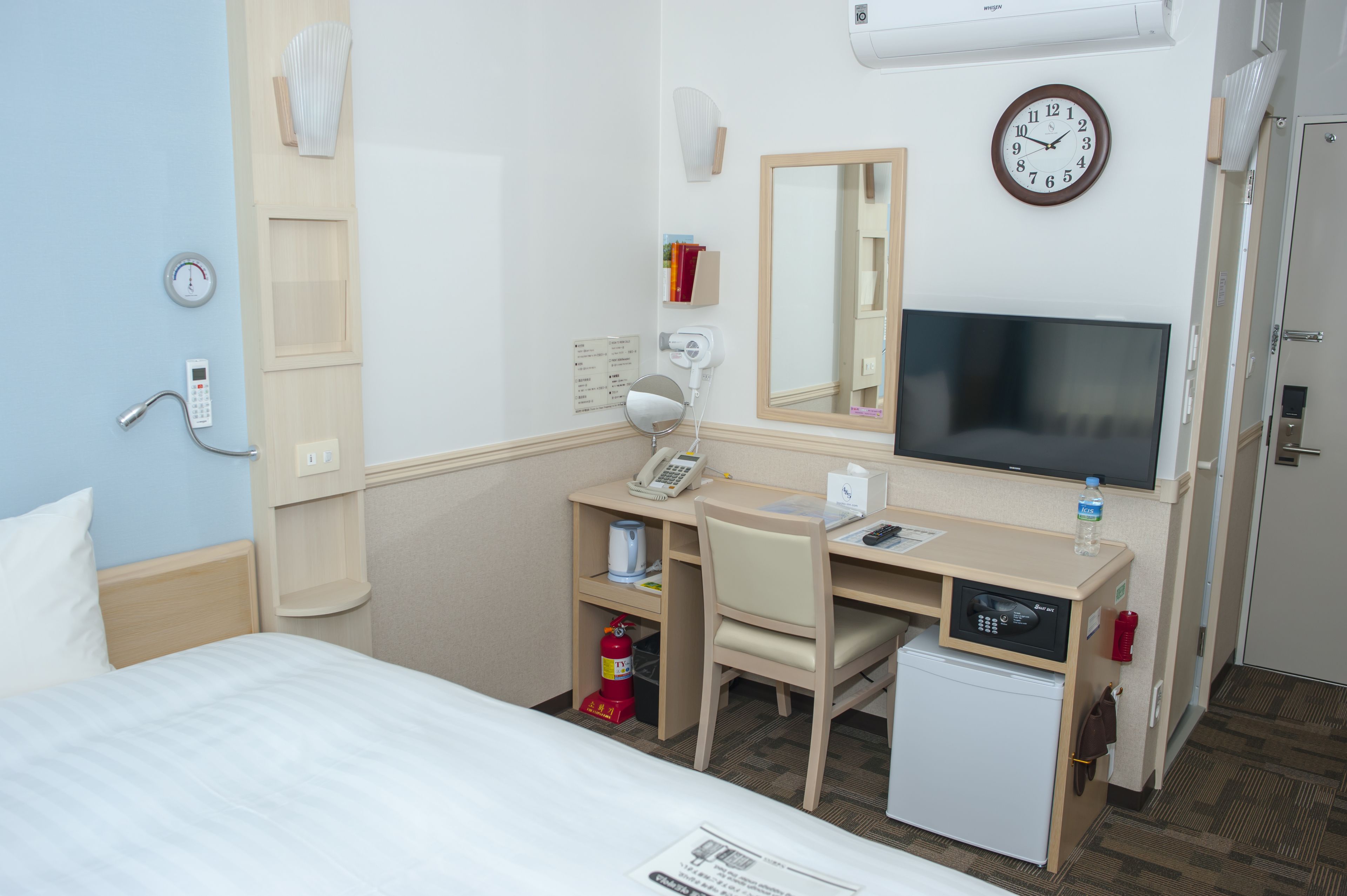 A hotel room with a bed, desk, chair, TV, and a small refrigerator.