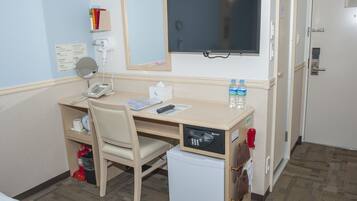 Habitación de hotel con escritorio, silla, espejo, refrigerador pequeño y televisor.