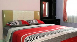 A bed with a patterned bedspread, a headboard, and a mirror above it. - Cendana Mulia Hostel (Bogor)