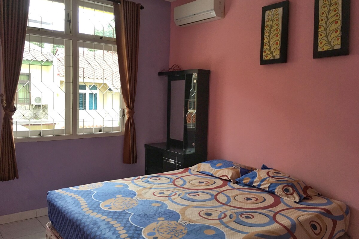 A bedroom with a bed, a dresser, and a window with curtains.