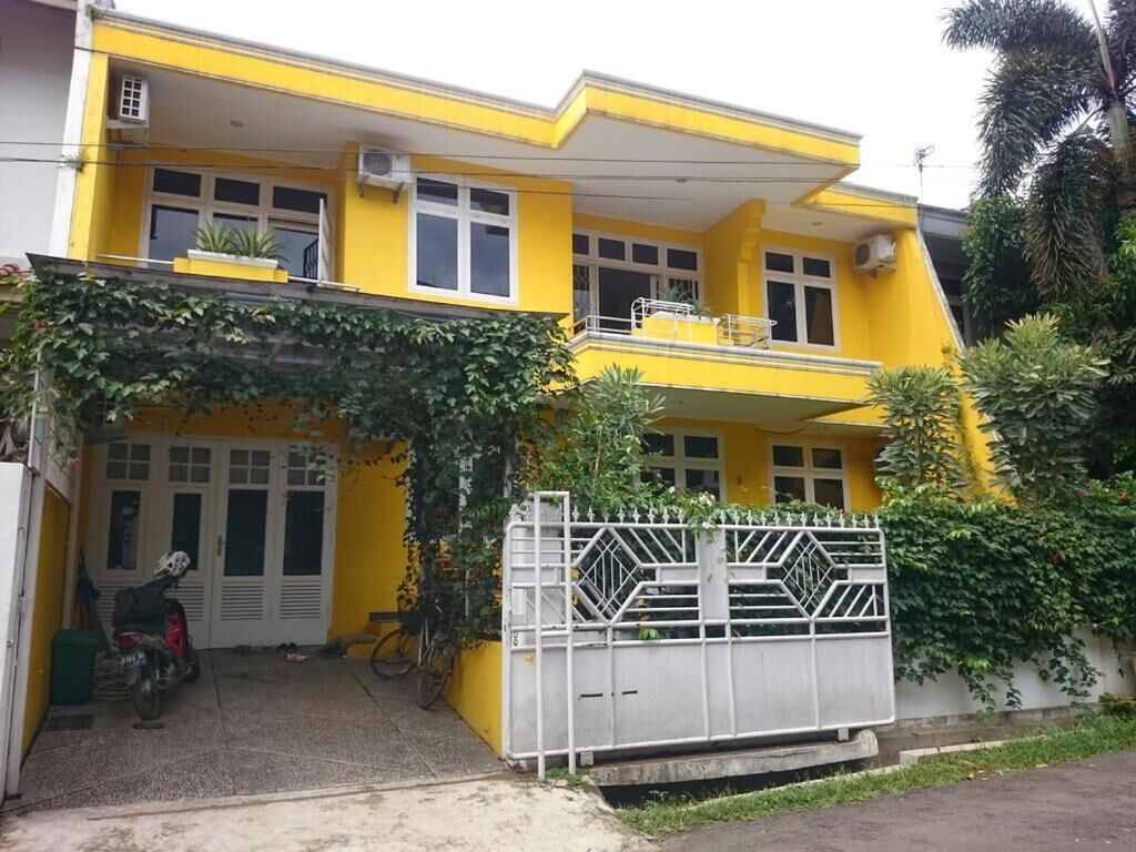 Een geel huis met twee verdiepingen, een balkon, een hek en een motorfiets voor de deur.