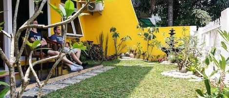 A courtyard with a yellow wall, a small garden, and a few people sitting on a bench.