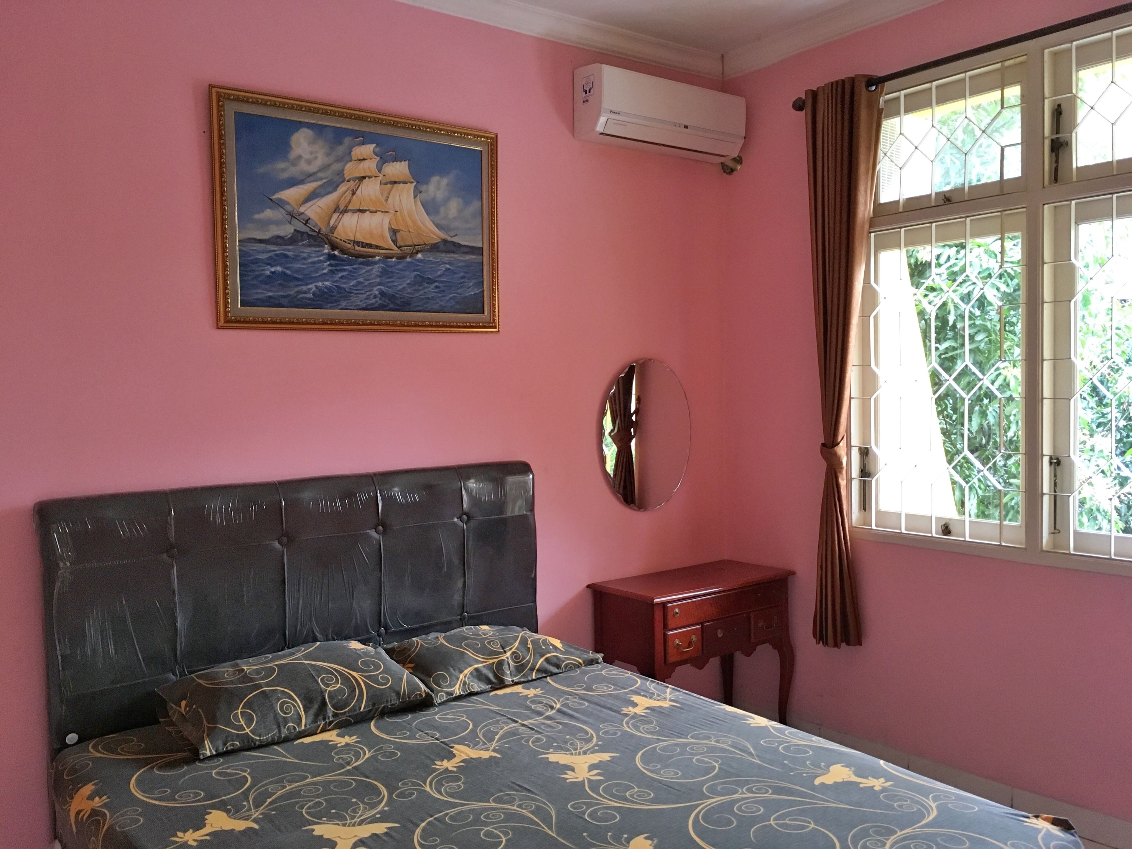Une chambre à coucher comprenant un lit, une table de chevet, un climatiseur fixé au mur, une fenêtre avec des rideaux et un tableau encadré représentant un navire.