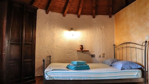 A bedroom with a bed, wooden wardrobe, and a wall-mounted shelf with a vase. - Tsolis Village (Aigialeia)