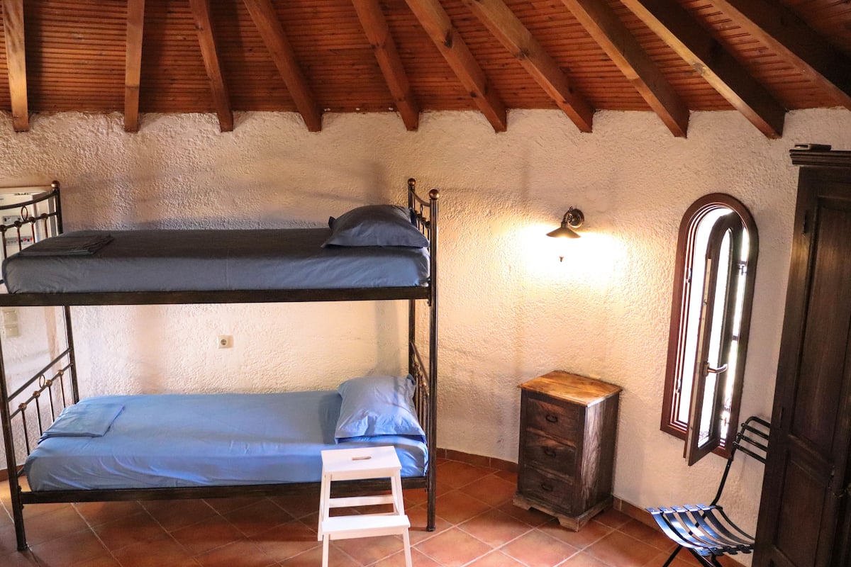 Un dormitorio con literas, un pequeño armario de madera, una silla y una ventana con espejo.