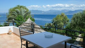 A balcony with a table and chairs overlooking a scenic view of the sea and mountains. - Tsolis Village (Aigialeia)