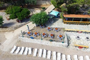 An outdoor seating area with tables and chairs, a bar, and a poolside lounge with sun loungers. - Tsolis Village (Aigialeia)