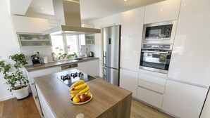 A modern kitchen with white cabinetry, a stainless steel refrigerator, an oven, and a built-in microwave. There is a wooden island with a fruit bowl and bananas. - Luxury Villa Petra near Split (Kastela)
