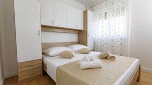 A neatly made bed with white linens and a beige bedspread, a wooden nightstand with a drawer, and a white wardrobe with a wooden accent. - Luxury Villa Petra near Split (Kastela)