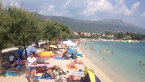 A beach with people sunbathing and swimming, umbrellas, and a clear sky. - Luxury Villa Petra near Split (Kastela)
