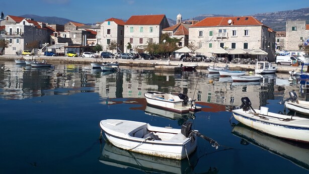 A harbor with boats docked, a stone building with a red roof, and a clear blue sky. - Luxury Villa Petra near Split (Kastela)