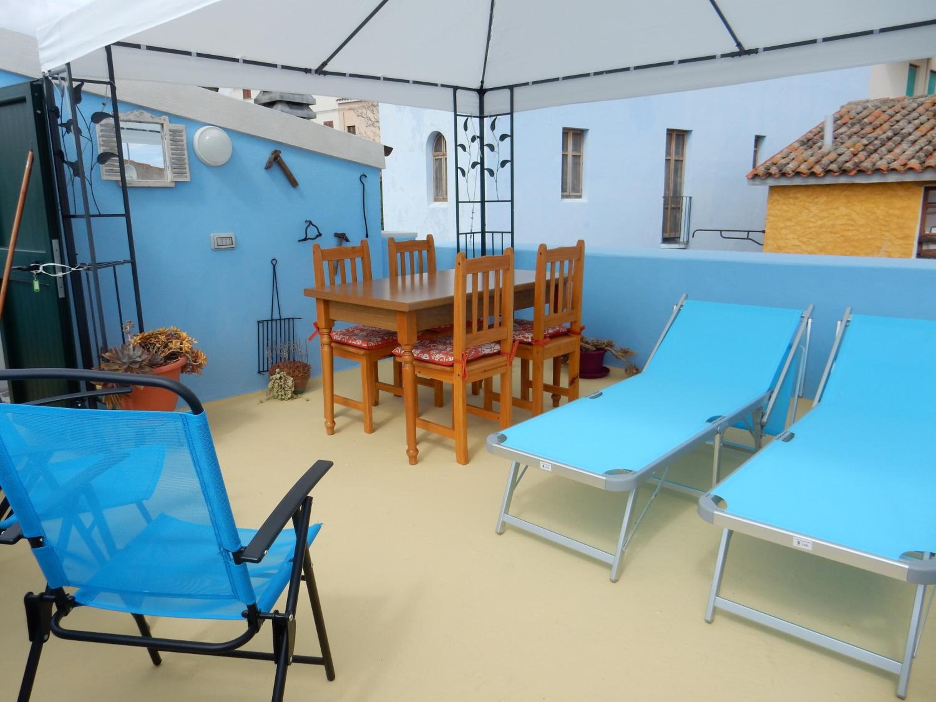 Una stanza con una parete blu, un tavolo da pranzo in legno con sedie, un tavolo pieghevole blu e una sedia pieghevole blu.