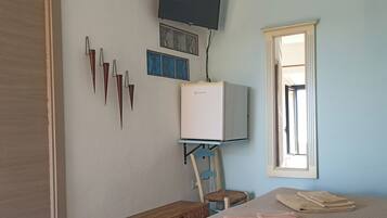 A bedroom with a bed, a TV mounted on the wall, a window, and a radiator.
