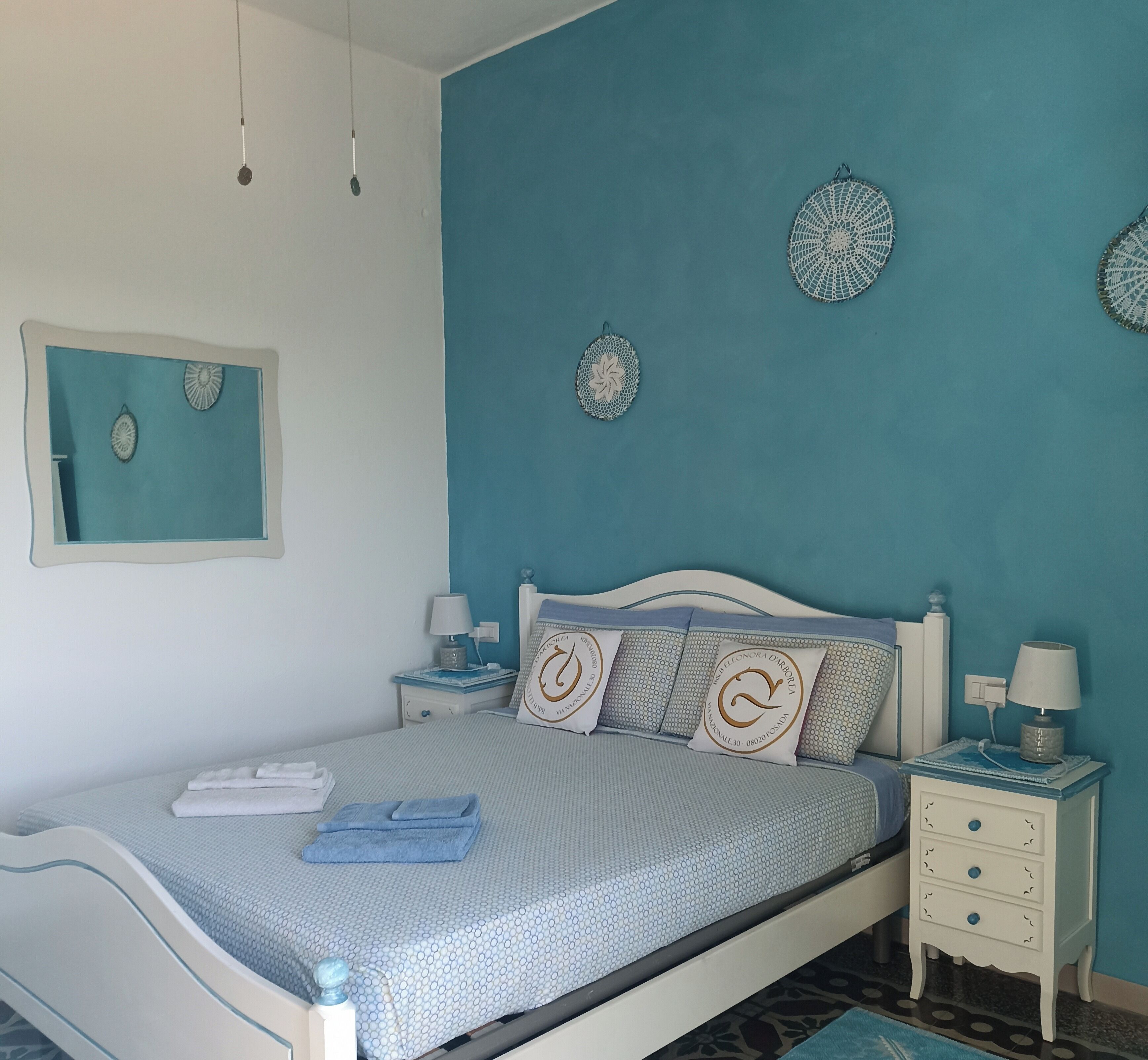 A neatly made bed with blue and white bedding, a bedside table with a lamp, and decorative wall art.