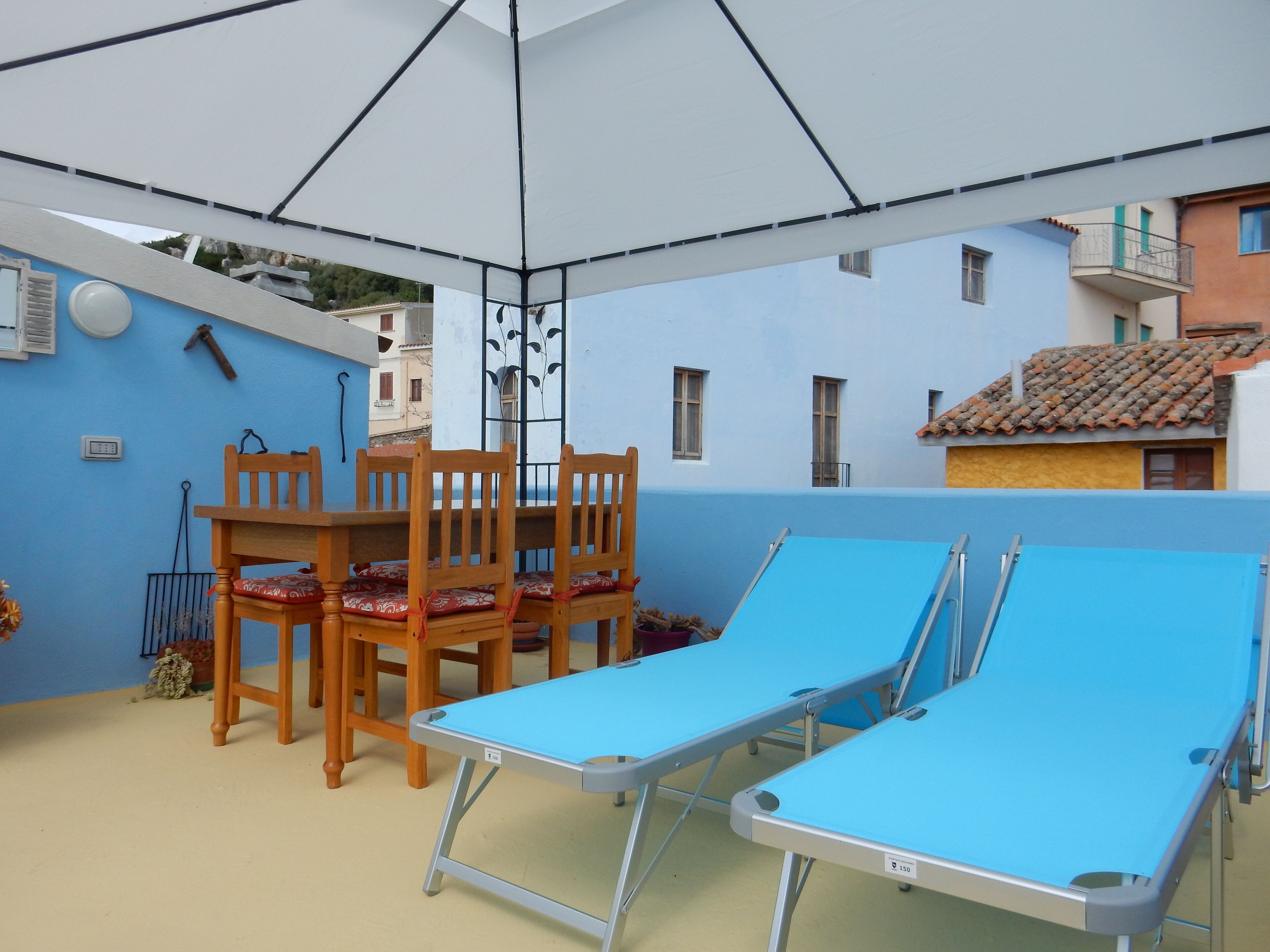 Un espace extérieur abrité, équipé d’une table et de chaises, de deux fauteuils bleus et d’un mur bleu.
