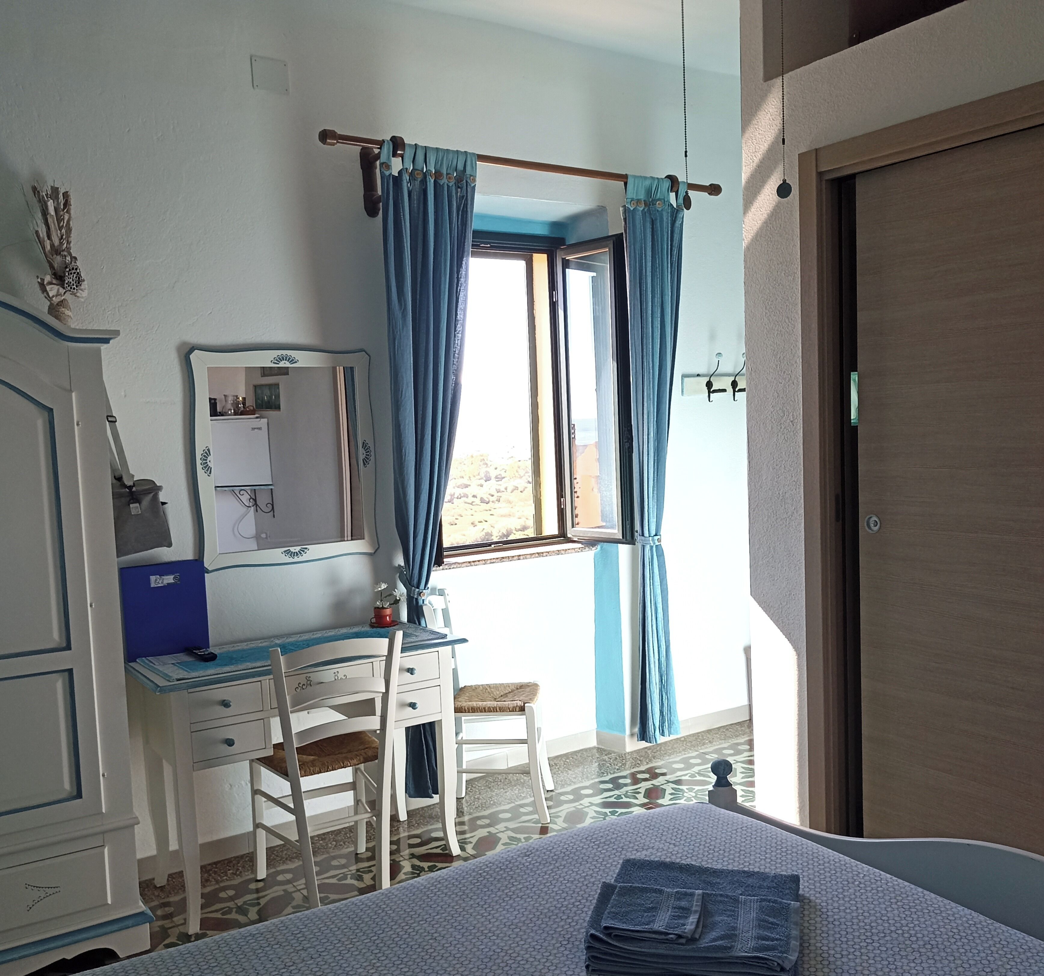 A bedroom with a bed, a desk, a chair, a wardrobe, a window with curtains, and a door.