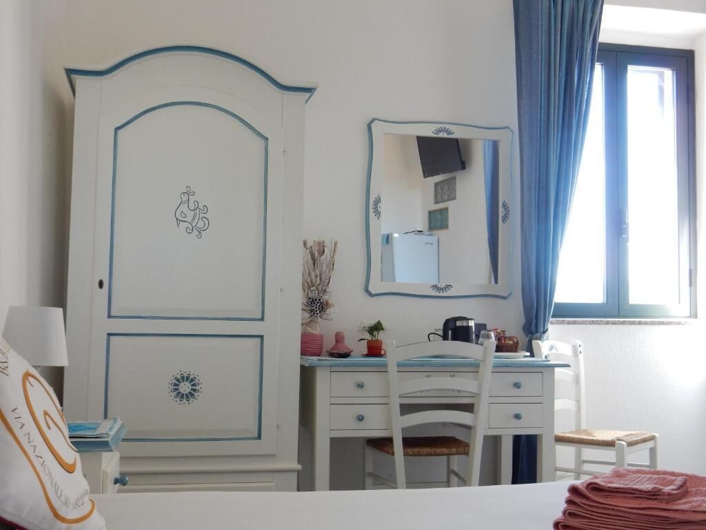 A bedroom with a bed, a white dresser with a mirror, a desk with a chair, and a window with curtains.
