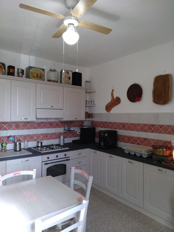 Una cocina con armarios blancos, estufa a gas, microondas y ventilador de techo.