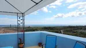 A balcony with blue chairs and a table, a potted plant, and a view of the sea and landscape. - B&B Eleonora D'Arborea (Posada)