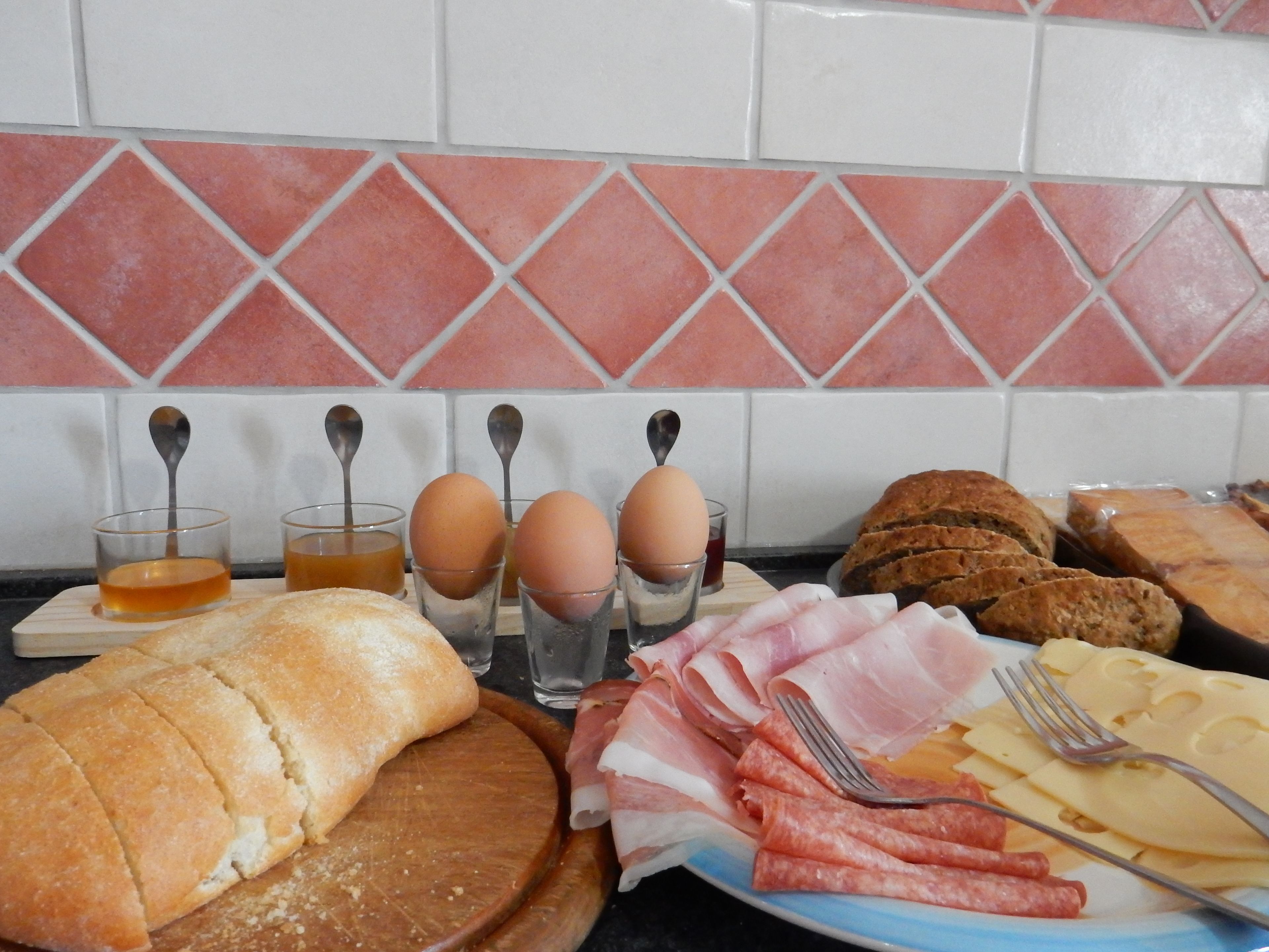 A breakfast spread with bread, eggs, ham, cheese, and a loaf of bread on a wooden board.