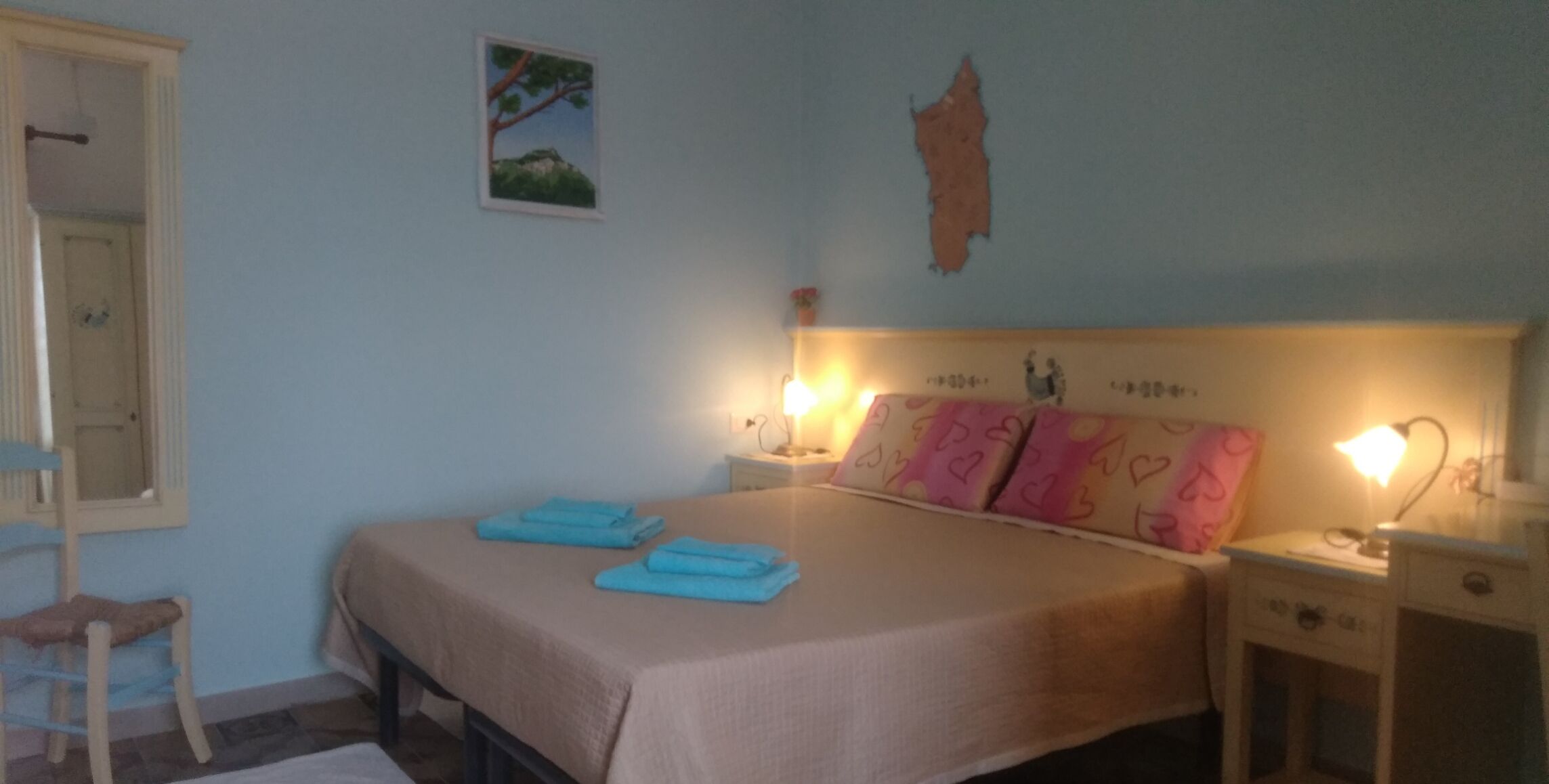 A bedroom with a bed, two bedside tables, a chair, a wall-mounted picture, and a wall decoration.