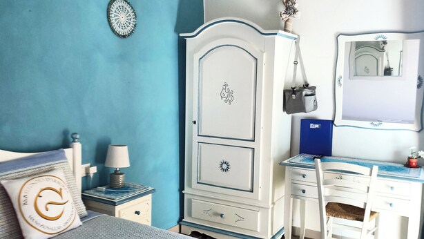 A bedroom with a bed, a desk, and a chair. There is a dresser with drawers and a mirror. - B&B Eleonora D'Arborea (Posada)