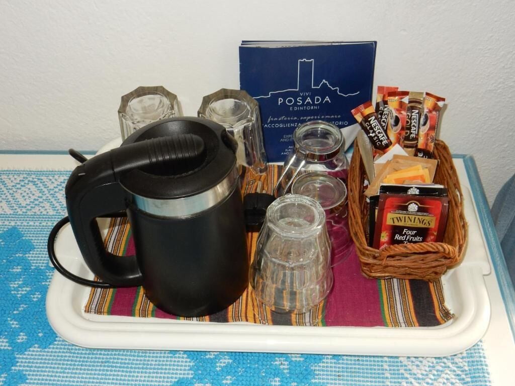 A tray with a black electric kettle, glassware, a box labeled 'Vivi Posada,' and a basket containing Twinings tea bags and red fruits.