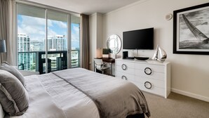 Ein Hotelzimmer mit einem großen Bett, einem Schreibtisch mit Stuhl, einem Fernseher und Blick auf die Stadt durch große Fenster.