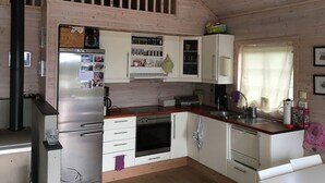 A compact kitchen with wooden beams, a refrigerator, a stove, and white cabinets. - Solferie Holiday Cottage Langenes (Kristiansand)