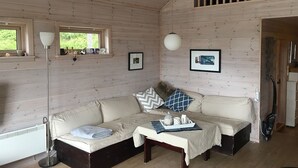 A cozy cabin interior with a sofa, a table with a tray of items, and framed pictures on the walls. - Solferie Holiday Cottage Langenes (Kristiansand)