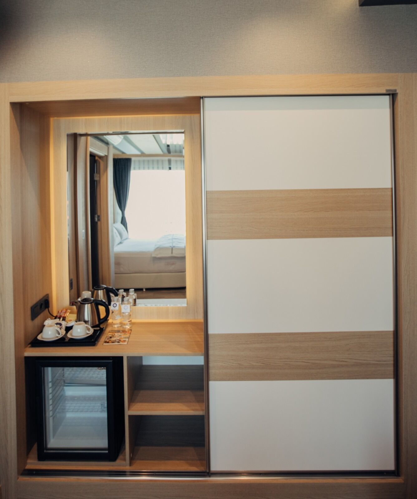 Een compacte kamer met een bed, een klein tafeltje met een waterkoker, bekers en een dienblad, plus een schuifdeur met een strepenpatroon.