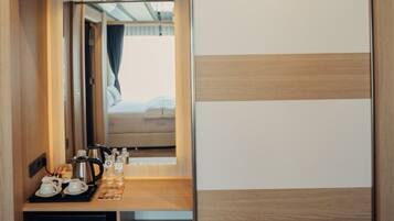 A compact room with a bed, a small table with a kettle, cups, and a tray, and a sliding door with a striped pattern.