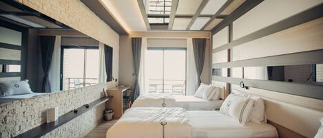A modern hotel room with a brick accent wall, a desk, two beds, and a large window with a view.