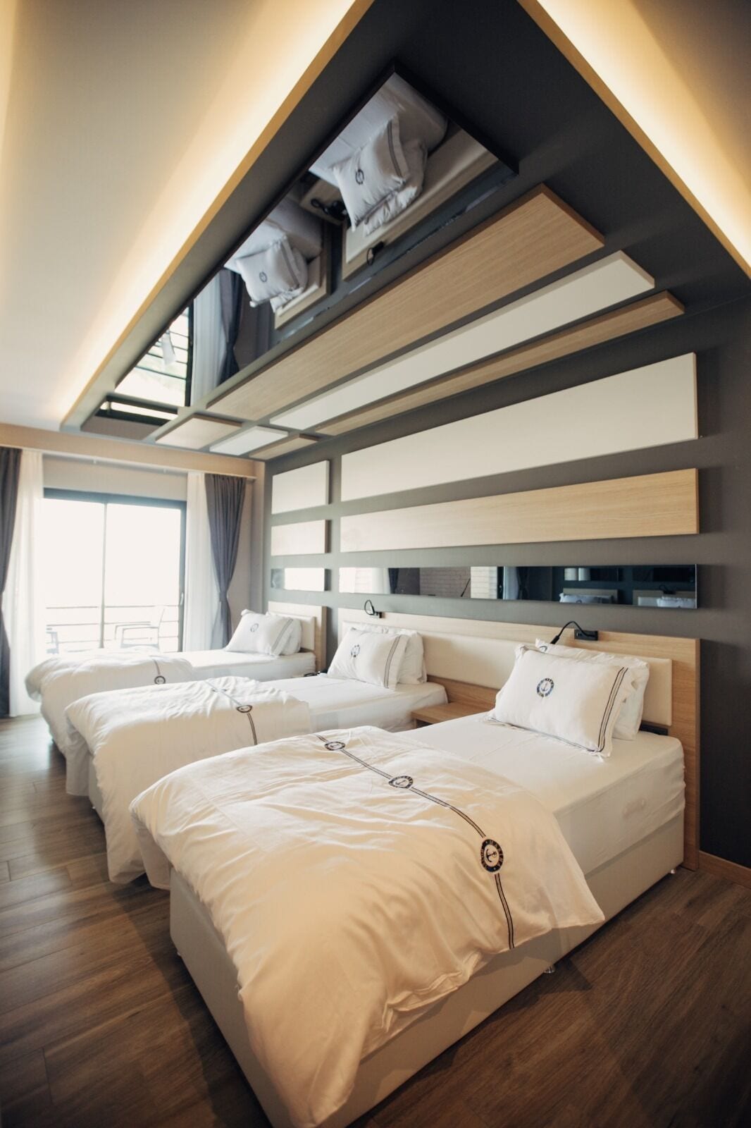 Habitación de hotel con tres camas, un tragaluz y suelo de madera.