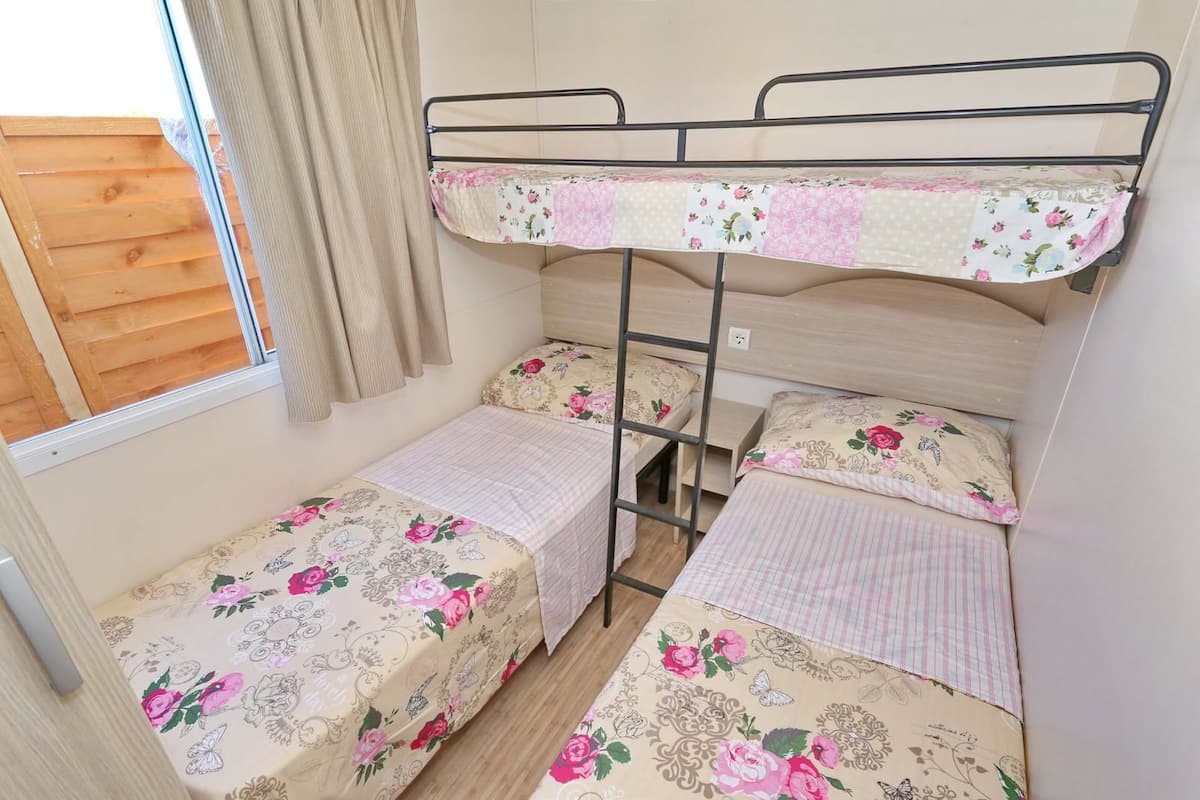 A bunk bed room with floral bedding and a wooden window blind.
