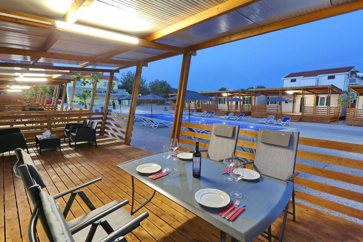 An outdoor dining area with wooden tables and chairs, overlooking a pool and beach area.