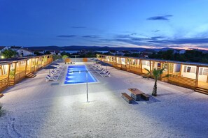 A pool area with lounge chairs and wooden cabins.