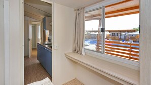 Een kamer met een groot raam met uitzicht op een zwembad, een kitchenette en een deur naar een andere kamer.