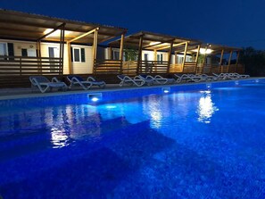 A swimming pool with lounge chairs and wooden structures with open sides.