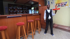 Un coin bar avec des tabourets en bois, un comptoir où sont exposées des bouteilles et une affiche accrochée au mur.