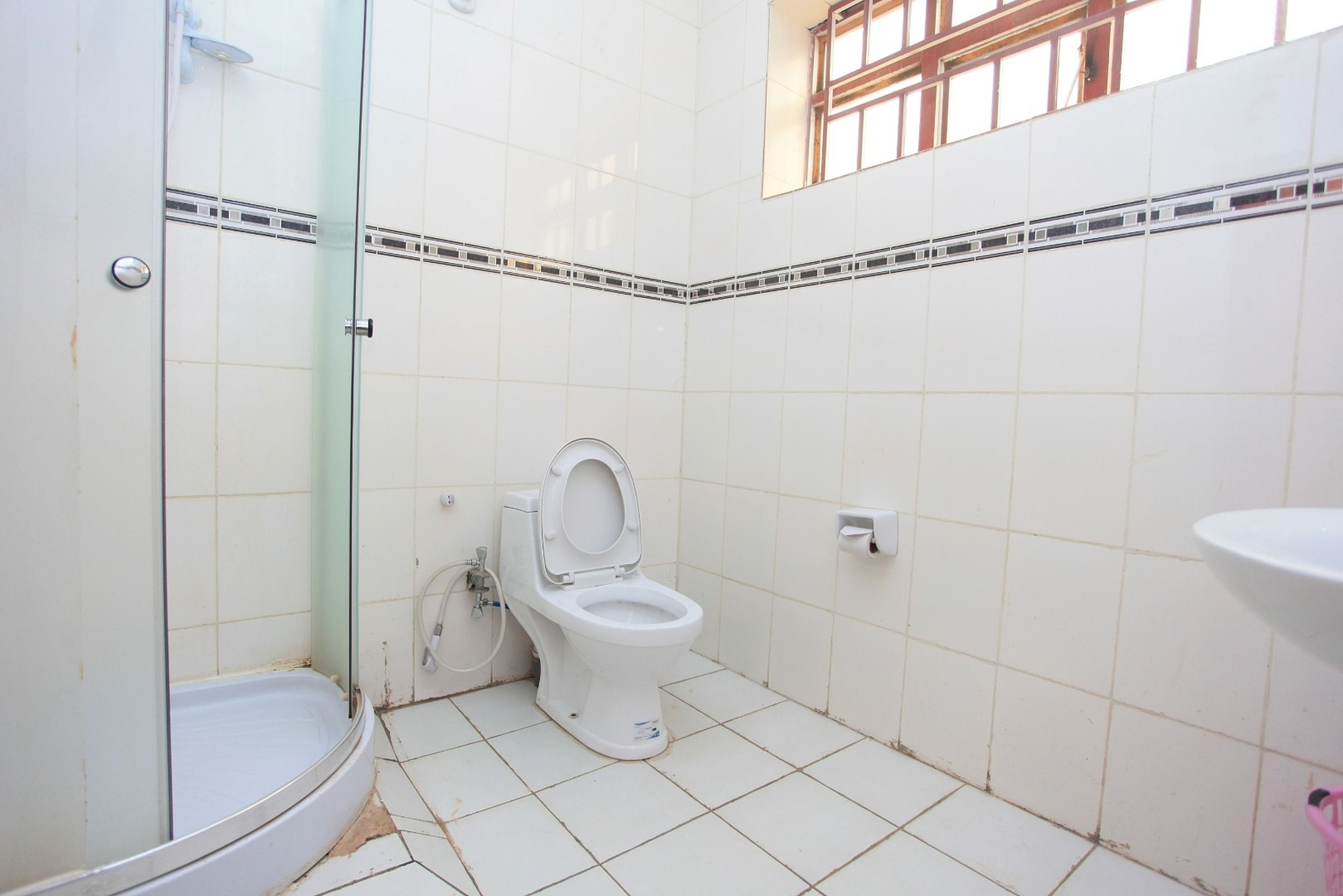 Un baño con azulejos blancos, inodoro, cabina de ducha de vidrio y lavamanos.