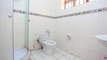 Un baño con azulejos blancos, inodoro, cabina de ducha de vidrio y lavamanos.