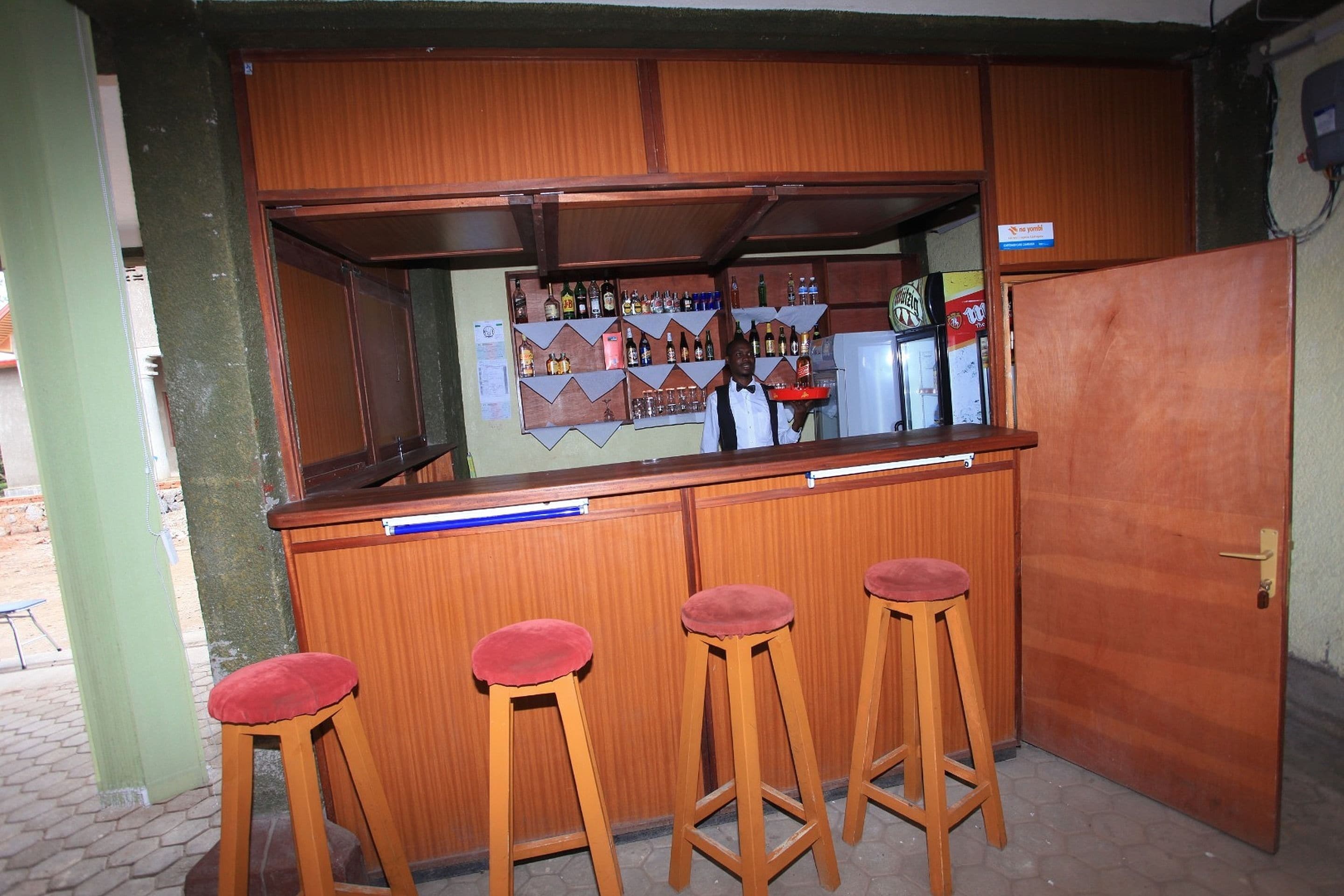 A bar area with wooden stools, a counter, and shelves stocked with bottles.