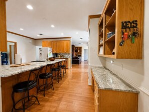 Een moderne keuken met houten kastjes, een marmeren aanrecht en een ingebouwde bar met barkrukken.