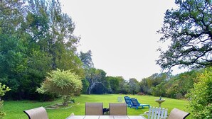 Une terrasse extérieure avec une table et des chaises, entourée d’une pelouse et d’arbres.