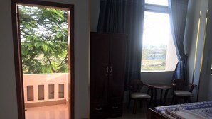 A room with a bed, a wardrobe, a small table with chairs, and a balcony with a view of trees. - Thanh Trinh Guest House (Binh Kien)