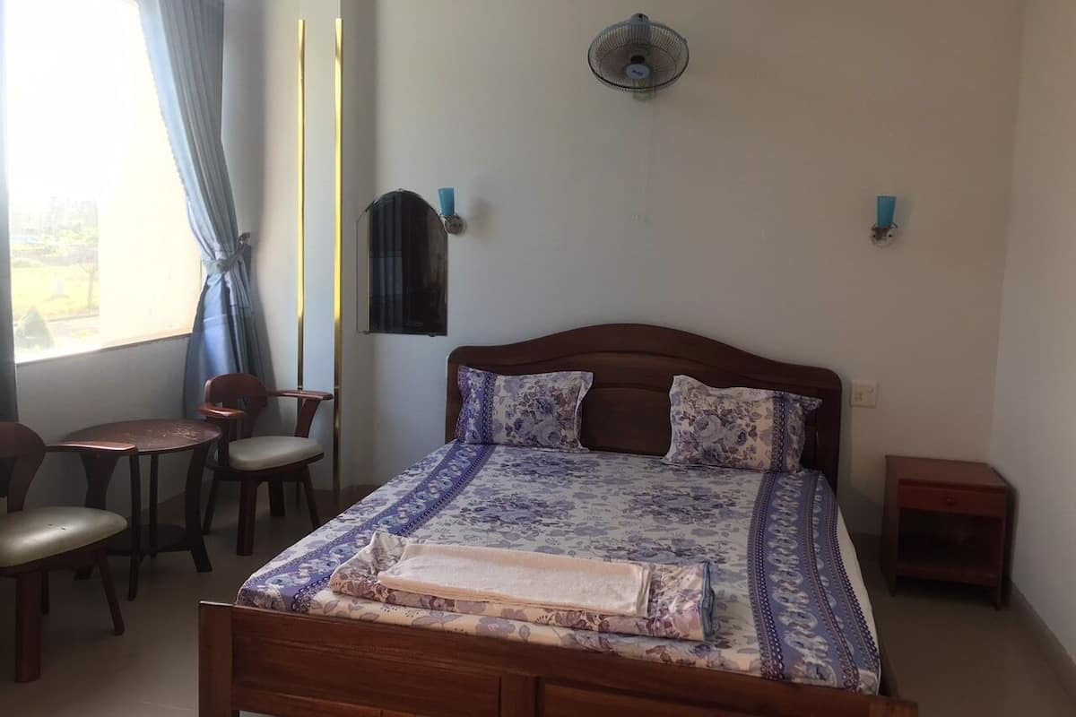 Une chambre à coucher comprenant un lit, une petite table, deux chaises, une table de chevet et une fenêtre avec des rideaux.