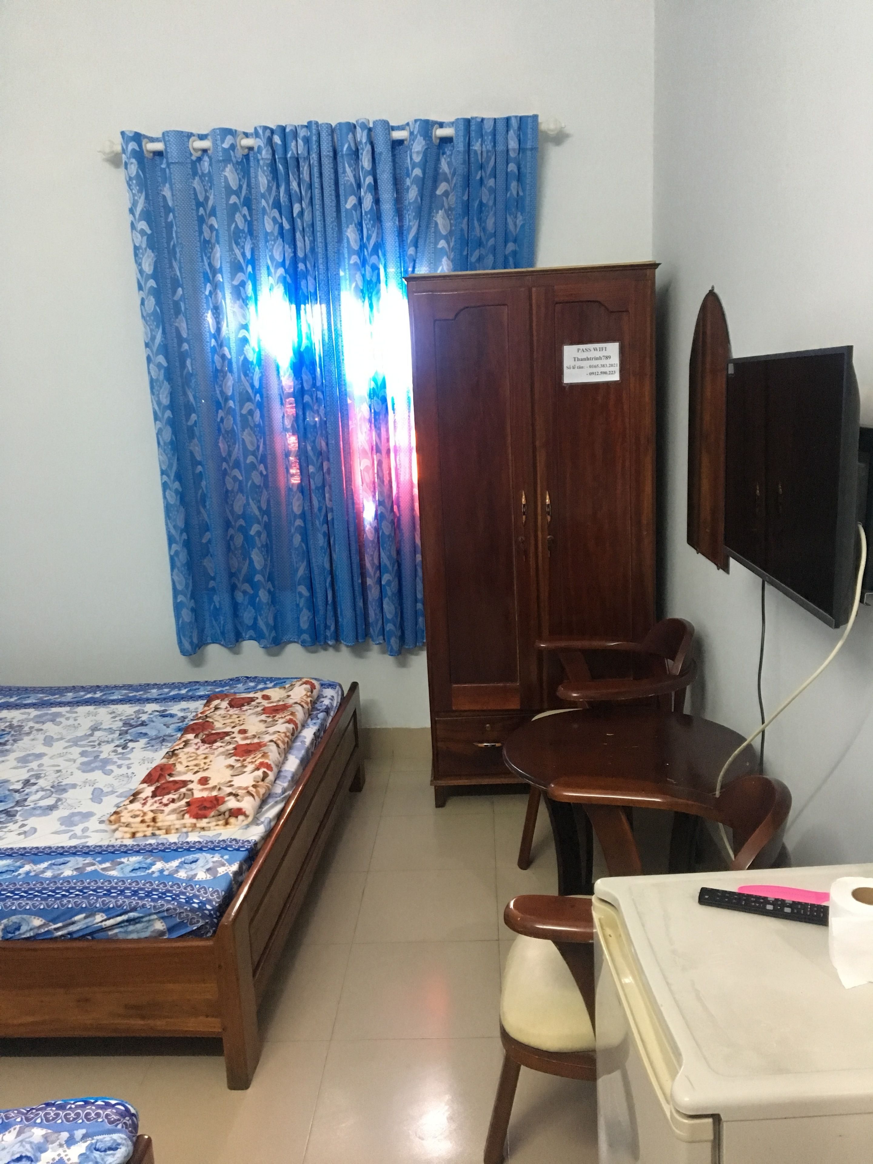 Un dormitorio con cama, un armario de madera, un escritorio con silla y un televisor montado en la pared.
